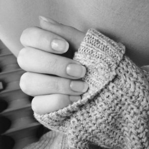 A black and white image of a ladies hand gently holding the cuff of her knitted sweater