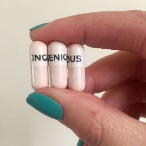 Three white collagen capsules with Ingenious written across them being held between two fingers