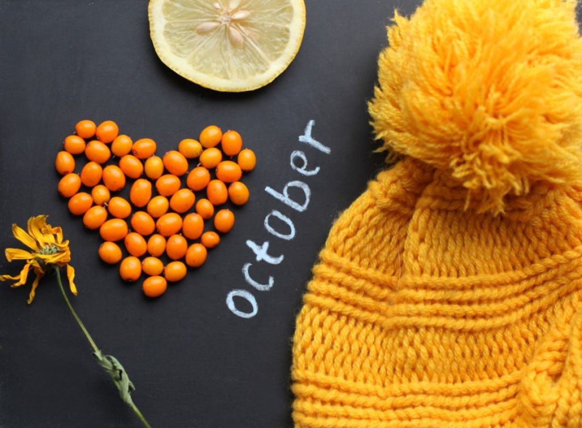 'October' is written in white chalk on a blackboard surrounded by various yellow items including a beanie, flower and lemon