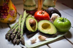 A selection of vegetables on a wooden surface including asparagus, avocado and tomatoes