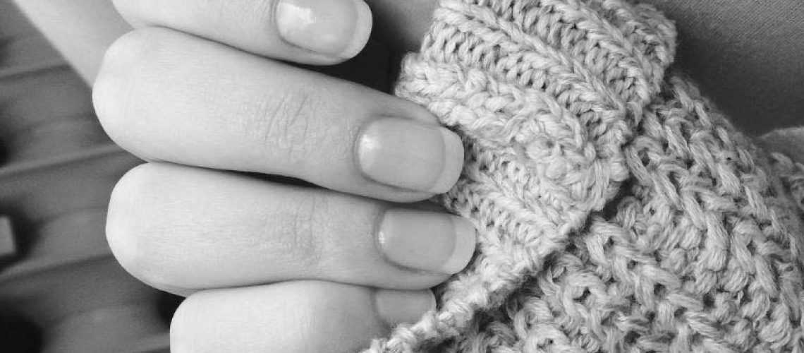 A black and white image of a ladies hand gently holding the cuff of her knitted sweater